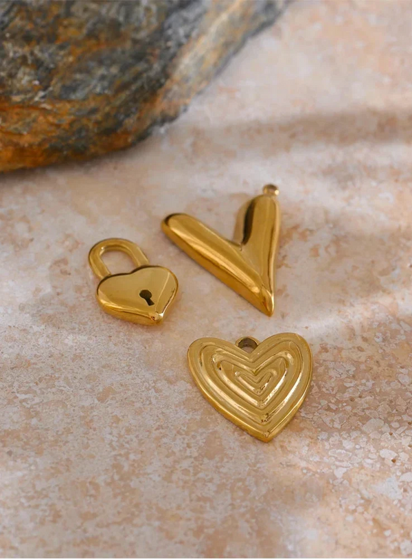 Three gold heart-shaped pendants on a textured surface