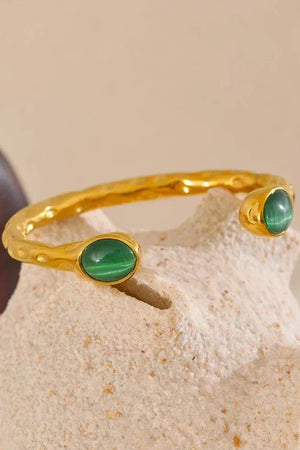 Gold bracelet with green stones on a textured beige surface