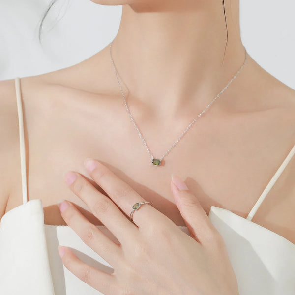 Close-up of a hand wearing a ring with a green gemstone on a light background
