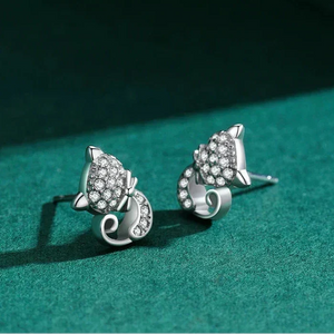 Silver cat-shaped earrings with clear stones on a green surface