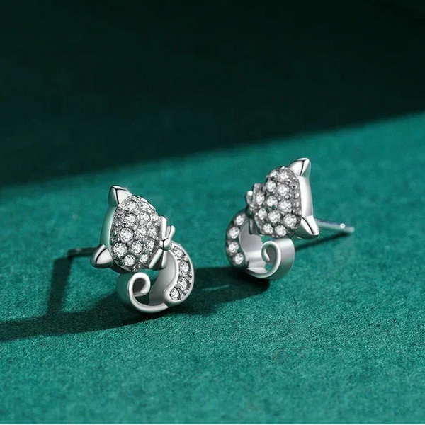Silver cat-shaped earrings with clear stones on a green surface