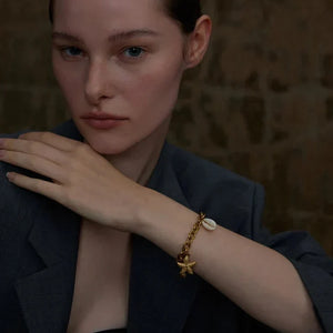 Woman wearing a dark blazer and gold bracelet with star design against a blurred background