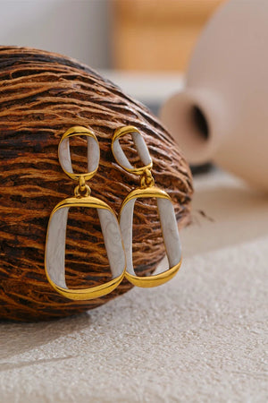 Gold and white earrings on a textured surface with a blurred background