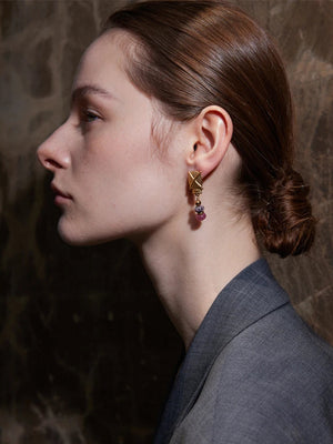 Close-up of a person wearing gold earrings with red stones against a dark background