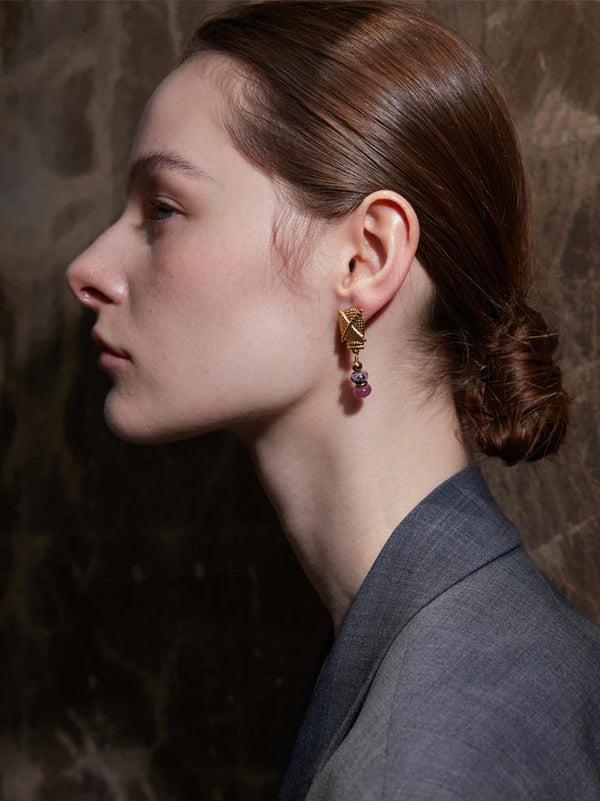 Close-up of a person wearing gold earrings with red stones against a dark background