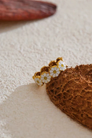 Gold ring with white floral designs on a textured beige surface