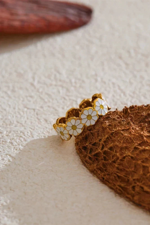 Gold ring with white floral designs on a textured beige surface