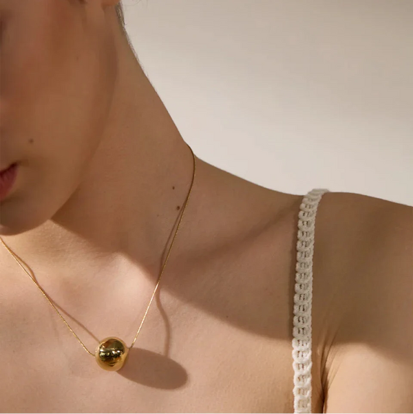 Close-up of a person wearing a delicate gold necklace with a small pendant.