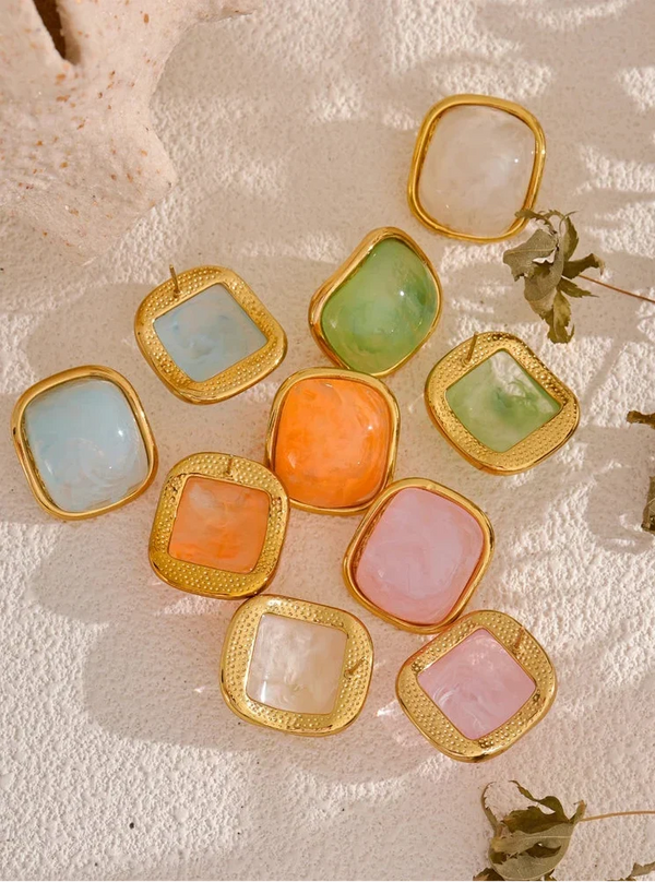 Colorful square earrings with gold frames on a textured surface