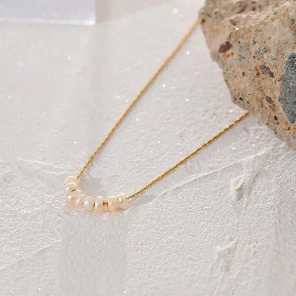 Gold-plated necklace with seven freshwater pearls on sandy textured background