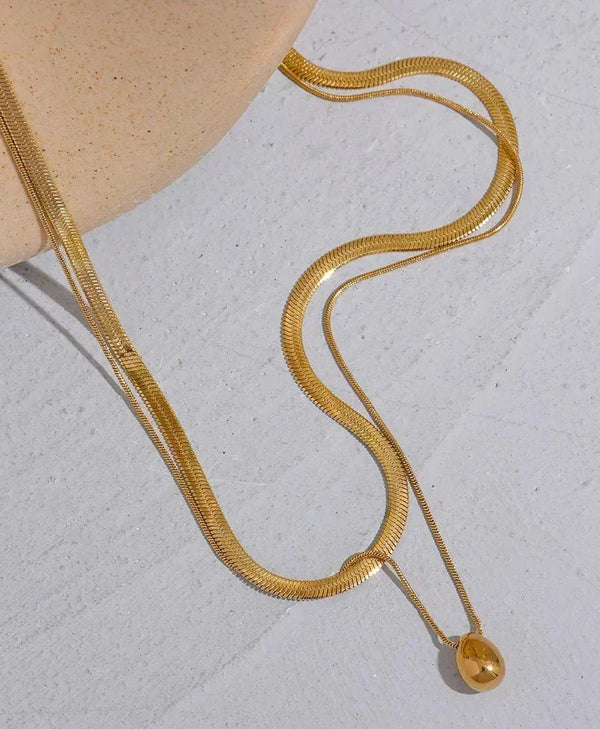18K gold-plated herringbone chain necklace with teardrop pendant on light surface