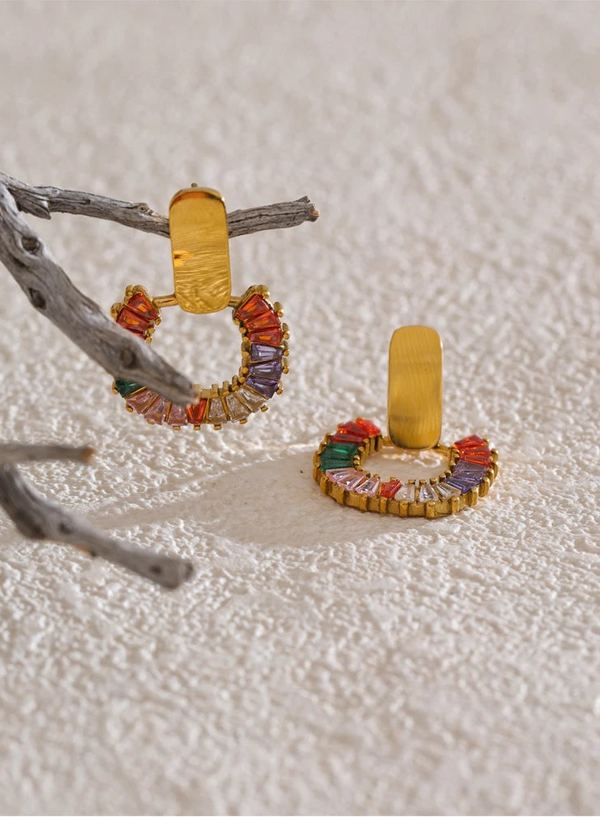 Colorful hoop earrings with gemstones on a textured white surface.