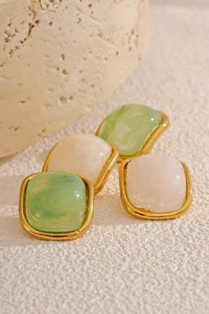 Pair of earrings with green and white stones on a textured beige surface