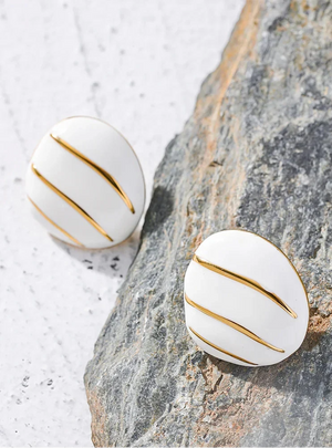 White earrings with gold stripes on a textured stone surface
