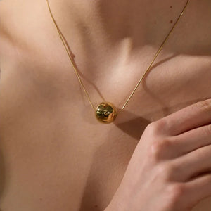 Gold necklace with a spherical pendant on a person's neck