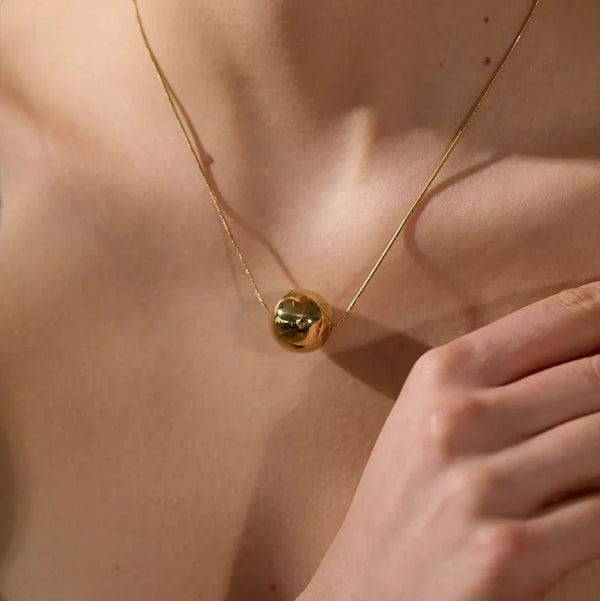 Gold necklace with a spherical pendant on a person's neck