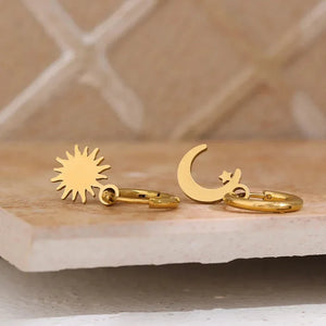 Gold sun and moon earrings on a marble surface with a neutral background