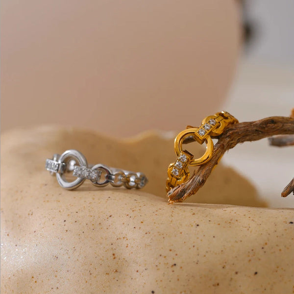 Two rings, one gold and one silver, on a textured beige surface.