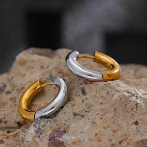 Two gold and silver hoop earrings on a textured stone surface with a blurred background.