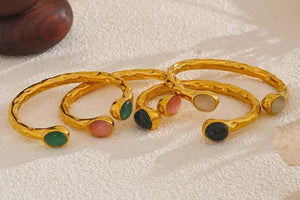 Gold bracelets with colorful stones on a textured surface, branded as Vogue.