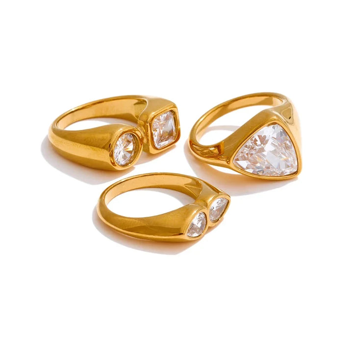 Three gold rings with clear gemstones on a white background.