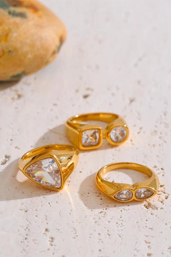 Three gold rings with clear gemstones on a textured surface