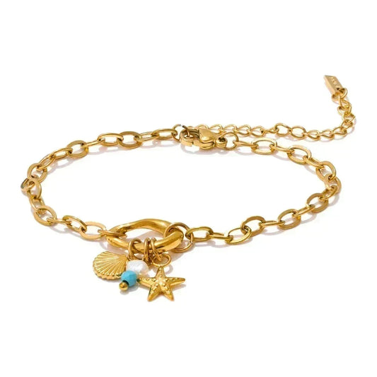 A gold chain bracelet with a lobster clasp and three charms: a scallop shell, a starfish, and a small turquoise bead, shown on a white background.
