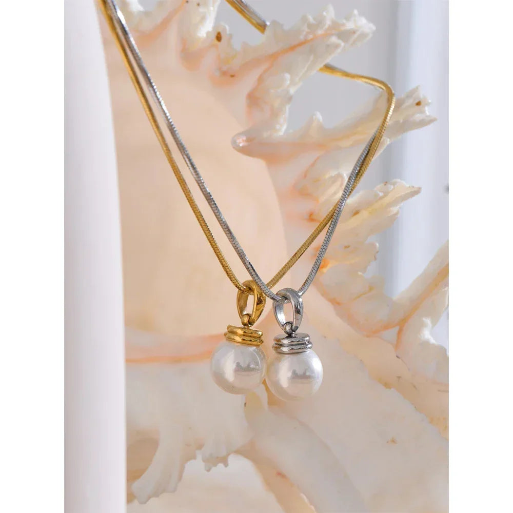 Two pearl pendants on gold and silver necklaces against a shell background