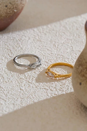 Two rings, one silver and one gold, on a textured beige surface.