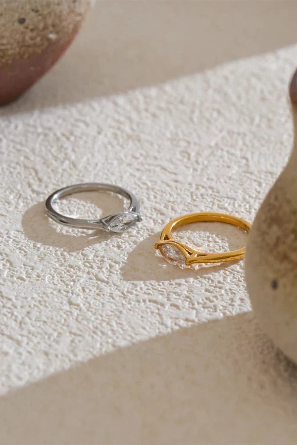 Two rings, one silver and one gold, on a textured beige surface.