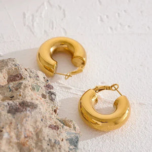 Chunky gold-plated hoop earrings on textured white surface with stone accent