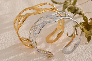 Gold and silver cuff bracelets on a textured surface with a plant in the background, featuring the Vogue logo.