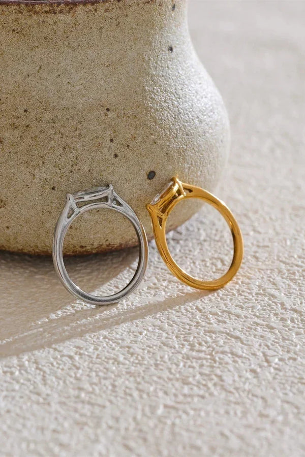 Gold and silver rings on a textured surface with a ceramic vase in the background