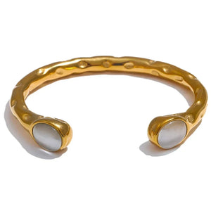 Gold bracelets with colorful stones on a textured surface, branded as Vogue.