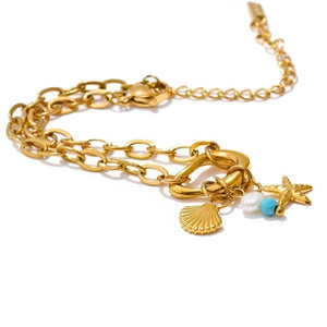 Gold bracelet with star, shell, and pearl charm on a white background