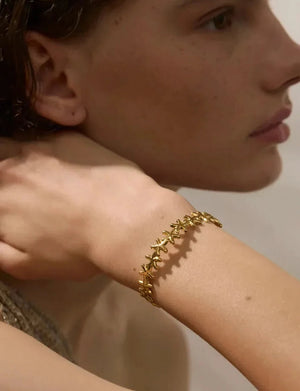Close-up of a person wearing a gold bracelet on a neutral background