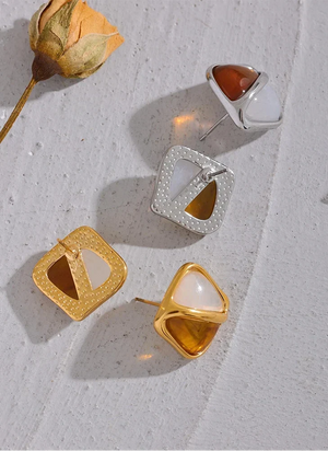 Gold and silver earrings on a textured surface with a dried flower.