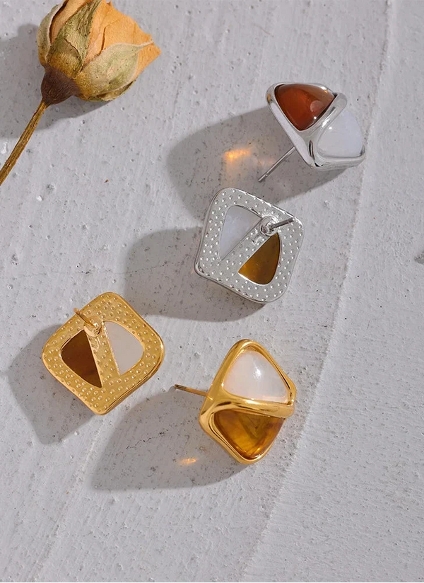 Gold and silver earrings on a textured surface with a dried flower.