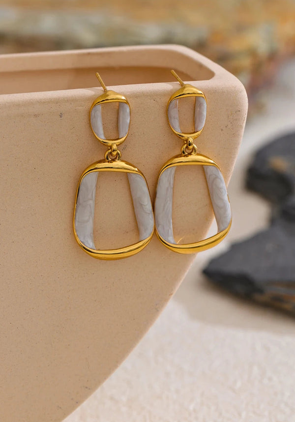Gold and stone earrings on a beige stand with blurred natural background