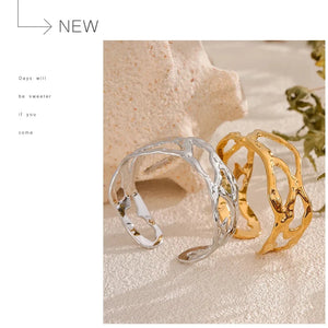 Two cuff bracelets, one silver and one gold, on a textured surface with a minimalistic background.