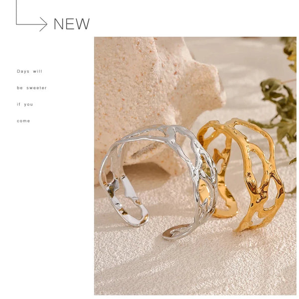 Two cuff bracelets, one silver and one gold, on a textured surface with a minimalistic background.