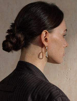 Woman with a stylish hair bun wearing gold earrings against a neutral background