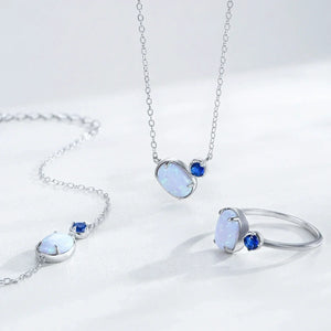 Silver jewelry set featuring a pendant necklace and matching ring, each with an oval white opal-like stone and a small round blue accent stone, displayed on a clean white background.