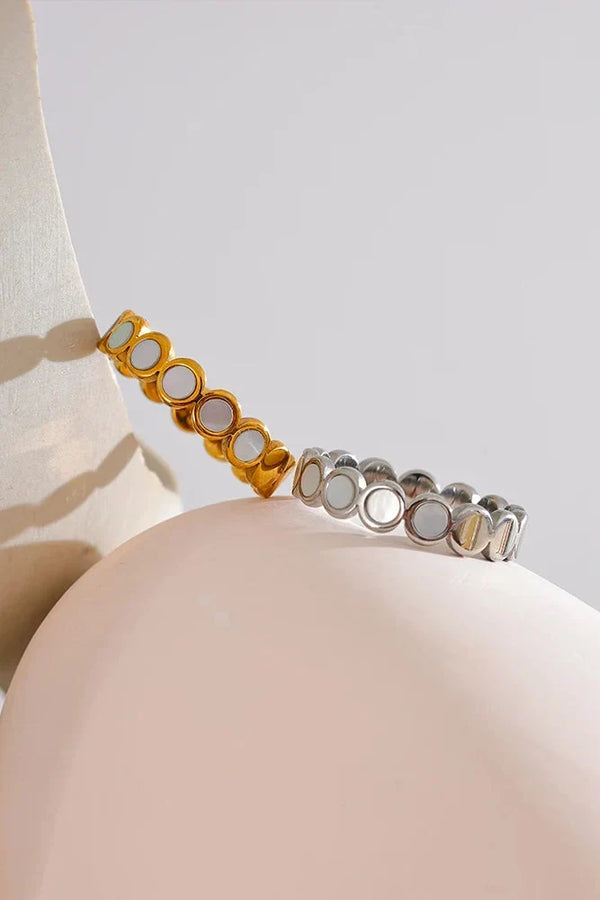 Two bracelets, one gold and one silver, on a neutral background