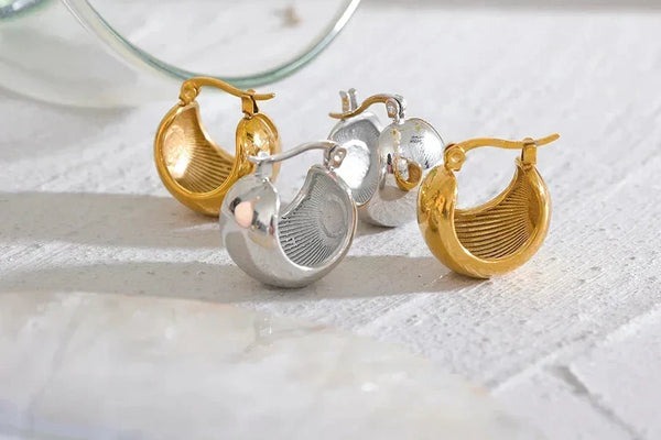 Pair of gold and silver chunky hoop earrings on textured white surface