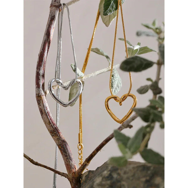 Silver and gold heart pendant necklaces displayed on a natural tree branch.