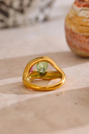 Gold ring with a green gemstone on a light wooden surface