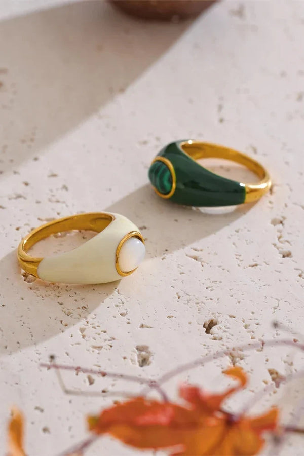 Two rings, one gold and one green, on a textured surface with blurred leaves in the background.