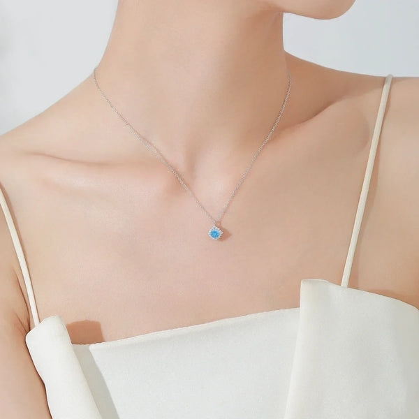 A close-up of a model wearing a delicate silver chain necklace with a small geometric pendant featuring a light blue center stone.
