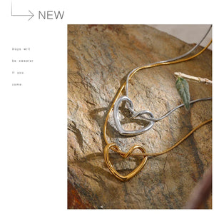 Heart-shaped gold and silver necklace on a stone surface with 'NEW' text above.